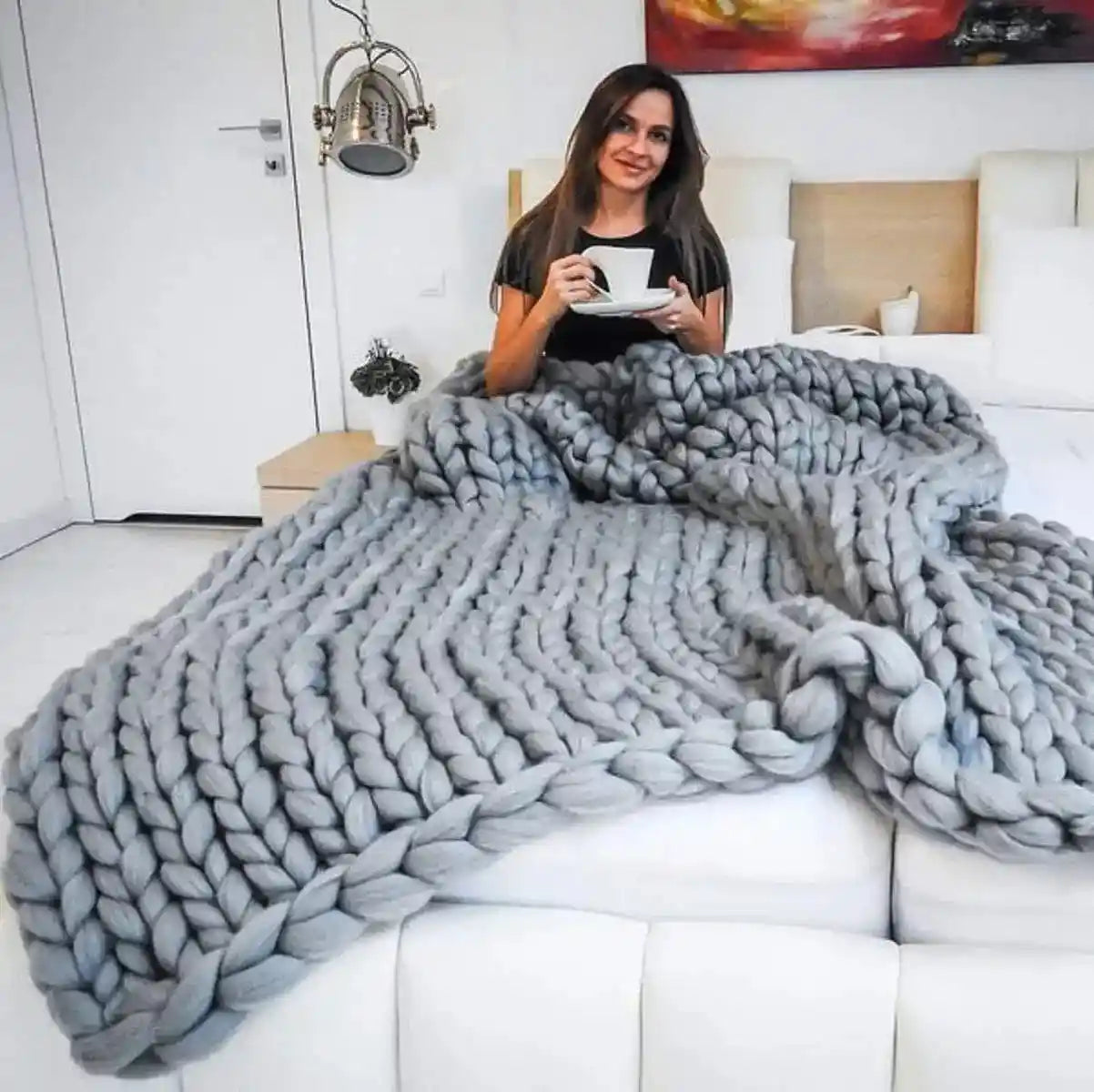 Gray chunky knit blanket on bed with person holding cup